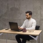 Seorang pria menggunakan laptop dan tablet di meja kerja minimalis untuk meningkatkan produktivitas.