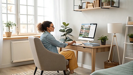 Wanita sedang bekerja santai di rumah minimalis sambil menggunakan laptop, fokus dan tenang