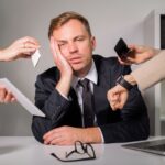 Seorang pria stres di kantor akibat kerja 12 jam sehari tapi tetap miskin, dikelilingi tekanan dari rekan dan tanggung jawab finansial